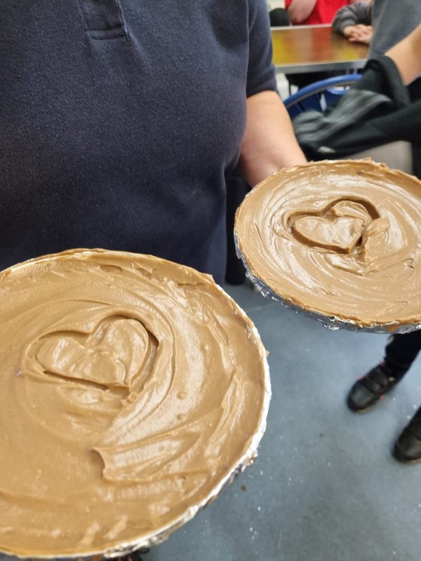 An adult, who can't be seen, holds up two large caramel tarts that have love hearts scored into the caramel