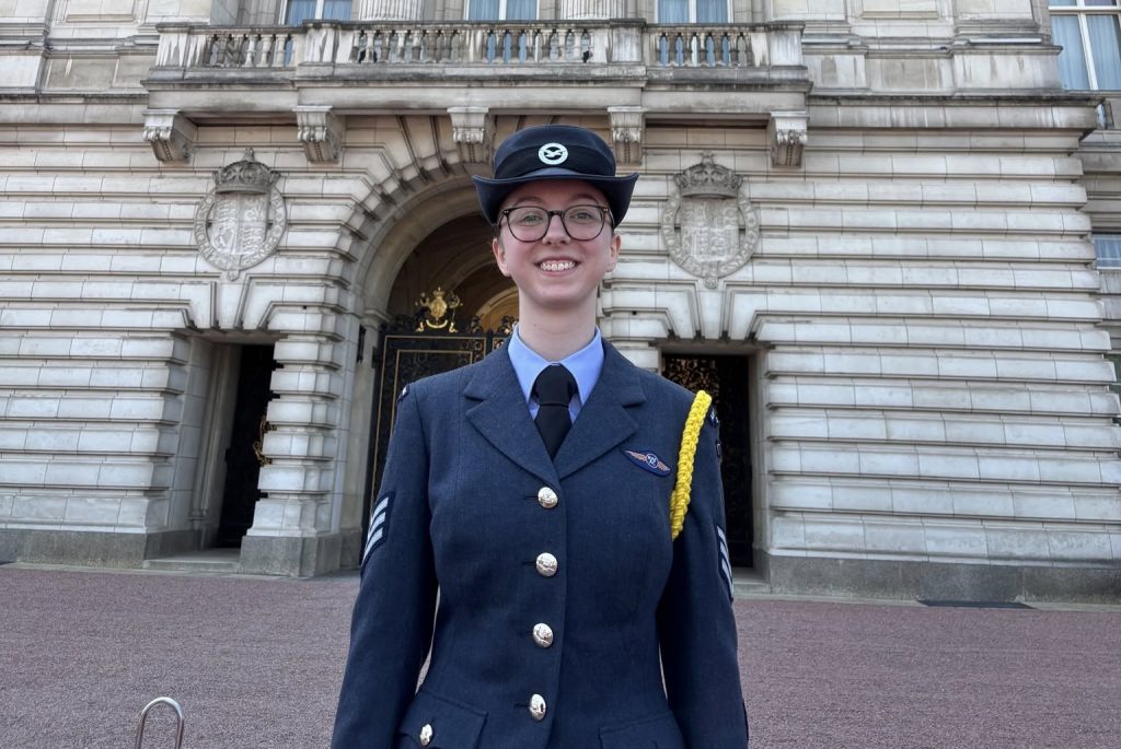 Gemma McGunnigle standing outside Buckingham Palace in her Air Cadets uniform, smiling at the camera